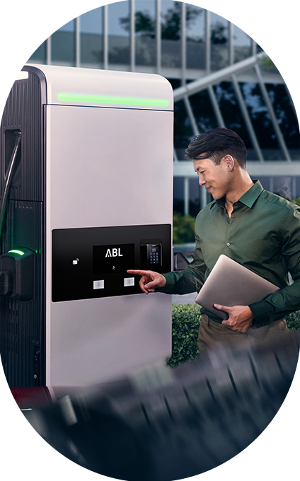 Telefonierender Mann steht neben Wallbox eMH1 mit Ladekabel für Elektrofahrzeuge in der Hand im Oval | ABL eMobility
